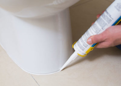 Close up of a plumber fixing toilet in a washroom with silicone cartridge