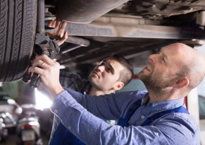 Two car mechanics checking up pressure in tires at garage